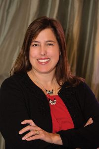 Headshot of Lori Halderman wearing red shirt under black cardigan against curtain background
