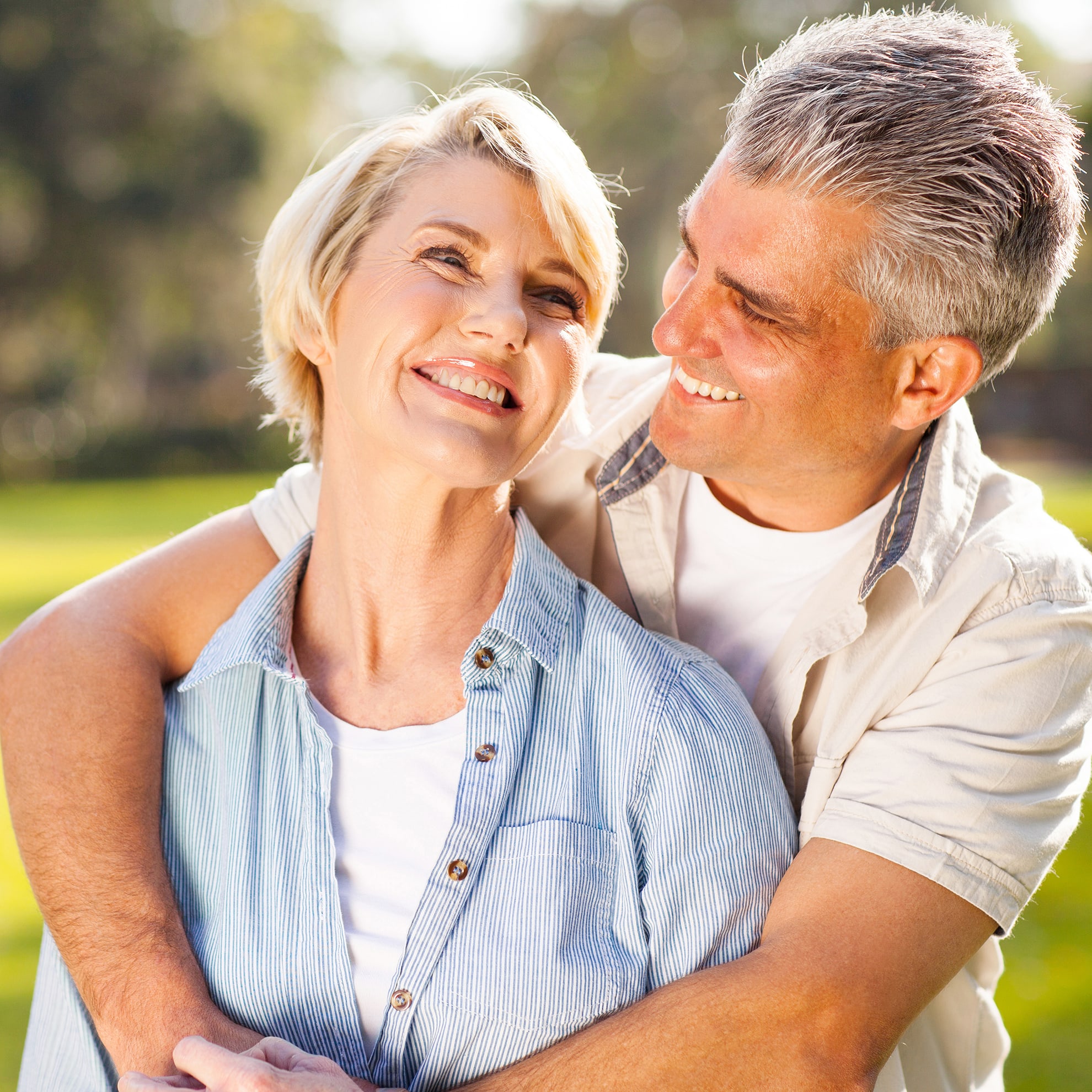 Older couple holding and looking at each other smiling against blurred out grass background