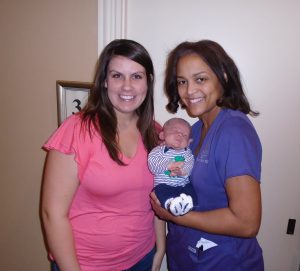 Woman in pink blouse posing next to nurse in purple scrubs holding newborn baby