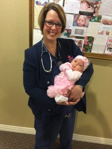 Nurse wearing navy blue scrubs holding newborn baby in pink outfit