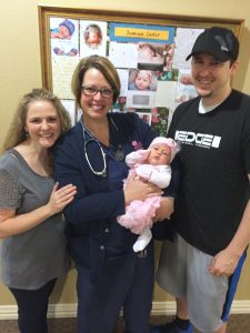 Woman posing with nurse holding her newborn baby next to father