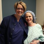 Pregnant woman in hospital gown and blue hair cap posing with nurse in navy blue scrubs