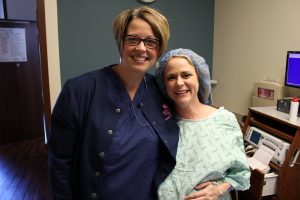 Pregnant woman in hospital gown and blue hair cap posing with nurse in navy blue scrubs