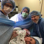 Woman right after giving birth in the delivery room with three others wearing blue hair-caps