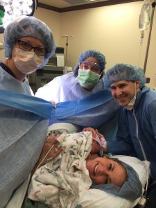 Woman right after giving birth in the delivery room with three others wearing blue hair-caps